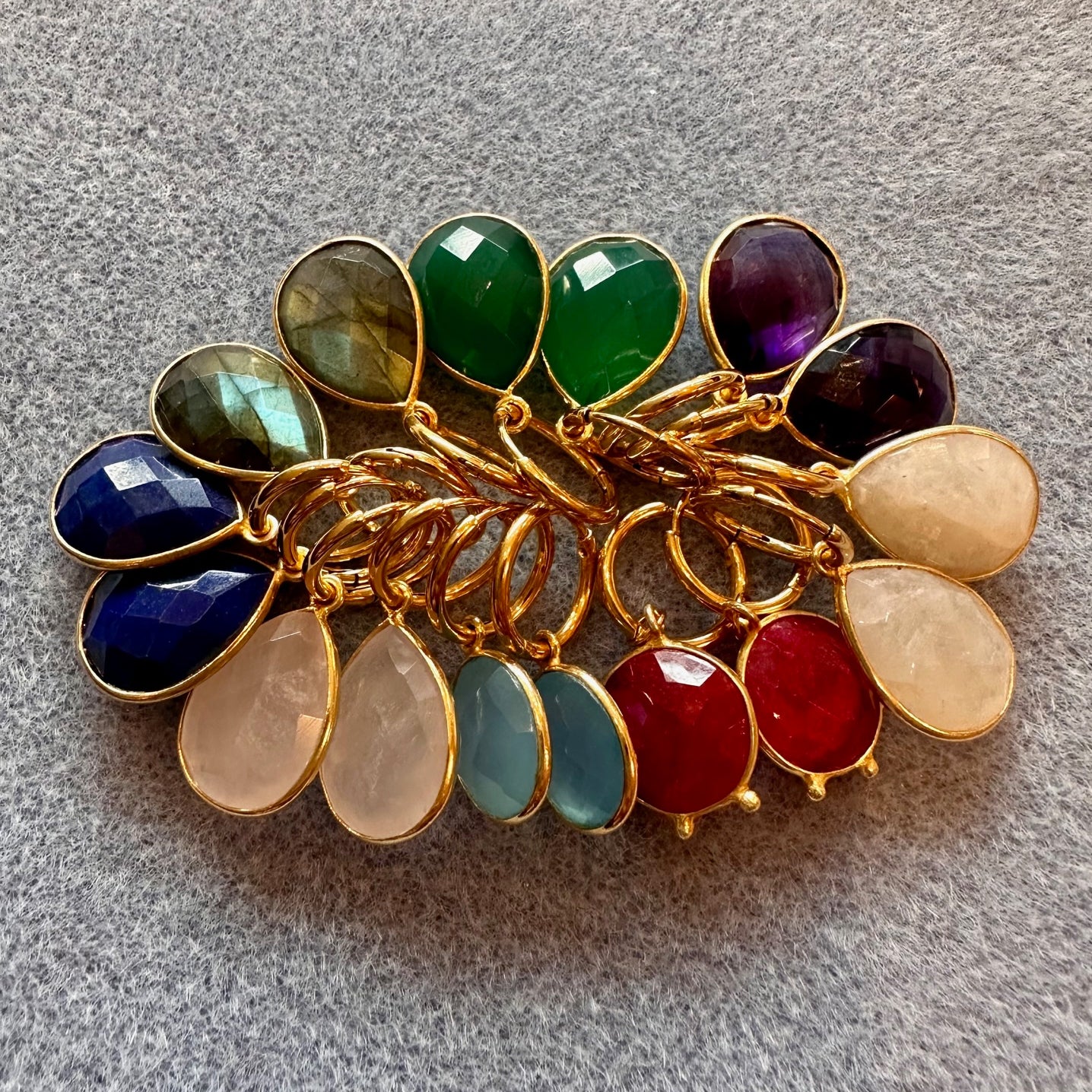 Gold hoop earrings with multicolored gemstone charms on a gray background