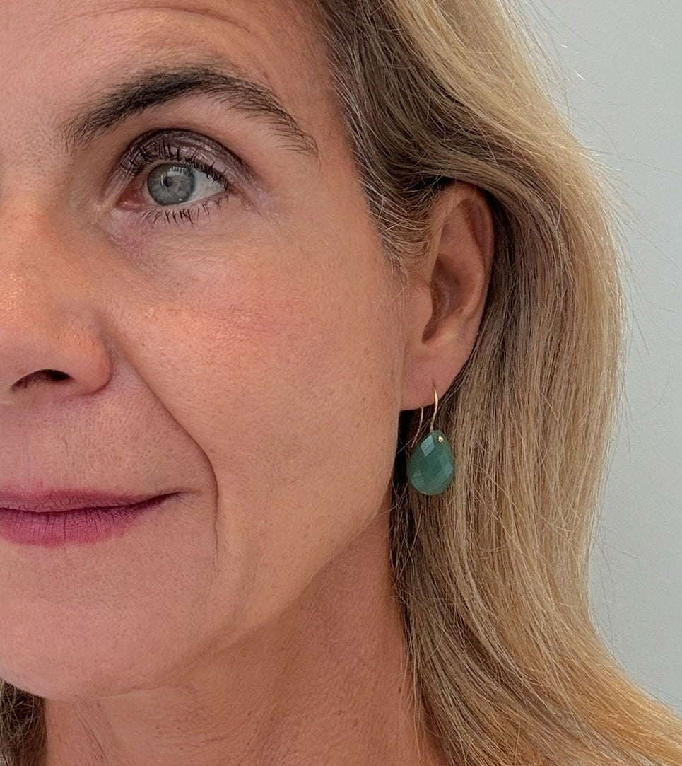 Close-up of a woman wearing aventurine teardrop earrings against a neutral background