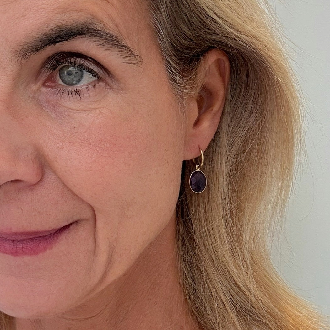Woman wearing gold hoop earrings with Amethyst oval charms