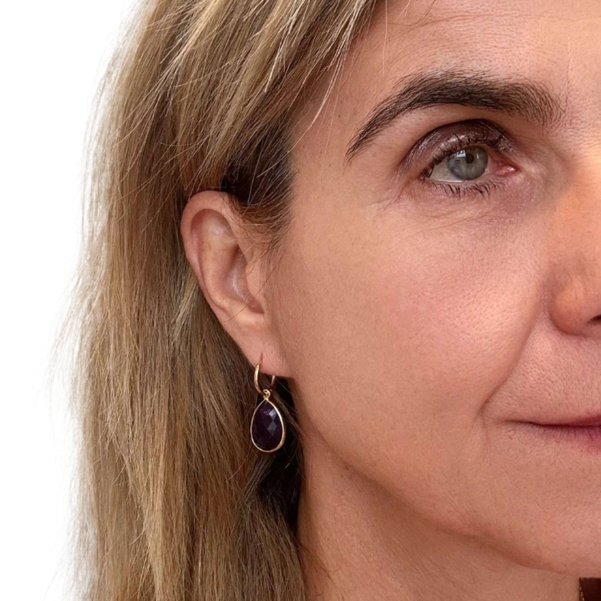 Close-up of a woman wearing a gold earring with a purple amethyst gemstone on a white background
