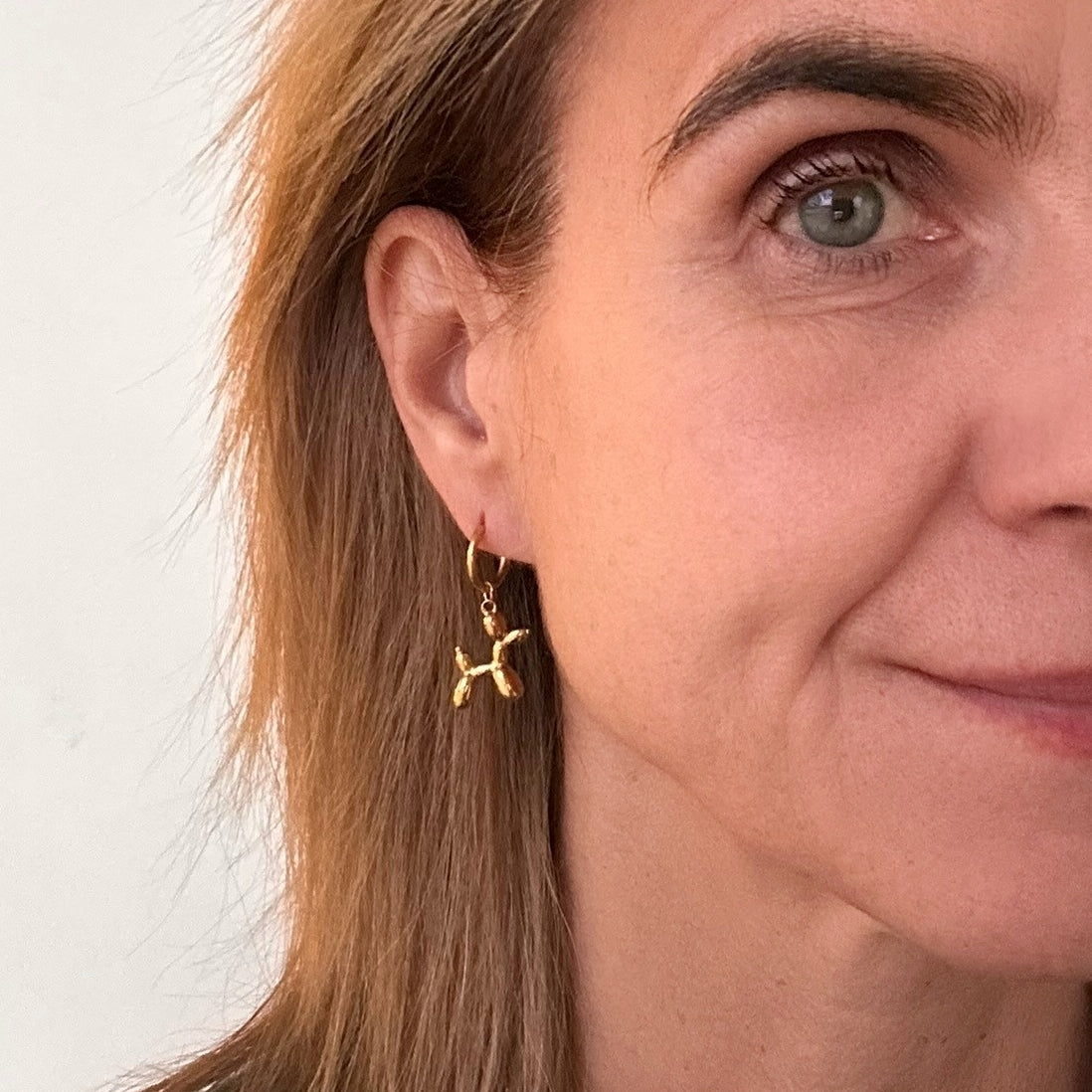 Delicate gold hoop earrings with Jeff Koons Balloon Dog charms on model
