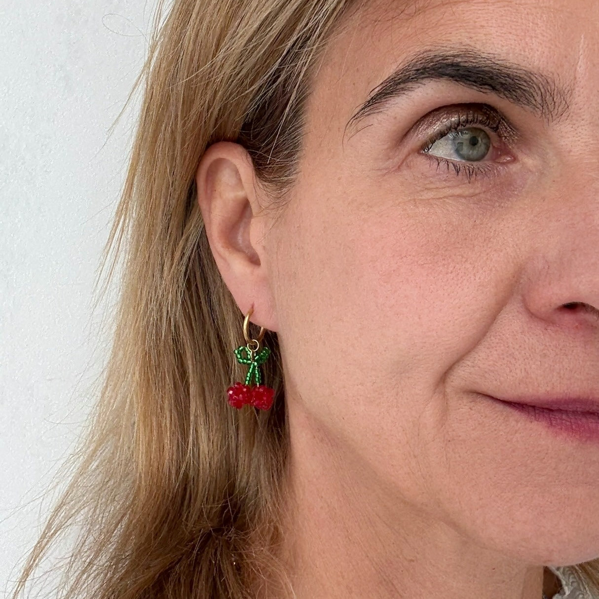 Delicate gold hoop earrings with beaded cherry charms on model