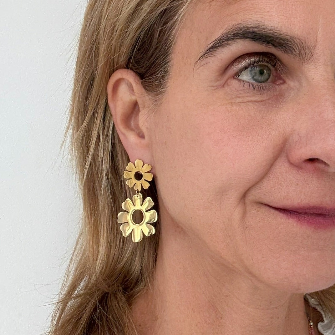 Big bold dangling gold earrings with two flowers with hole in the middle worn on model