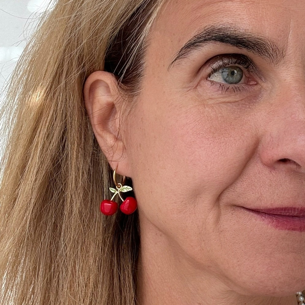 Delicate gold hoop earrings with big red cherry shaped charms on model