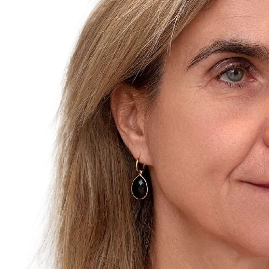 Close-up of a woman wearing a gold earring with a black agate gemstone on a white background