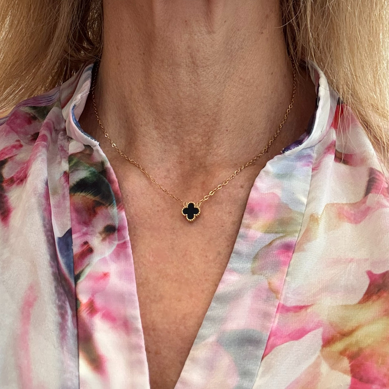 Delicate gold chain necklace with tiny 9mm black clover charm in the middle worn on model