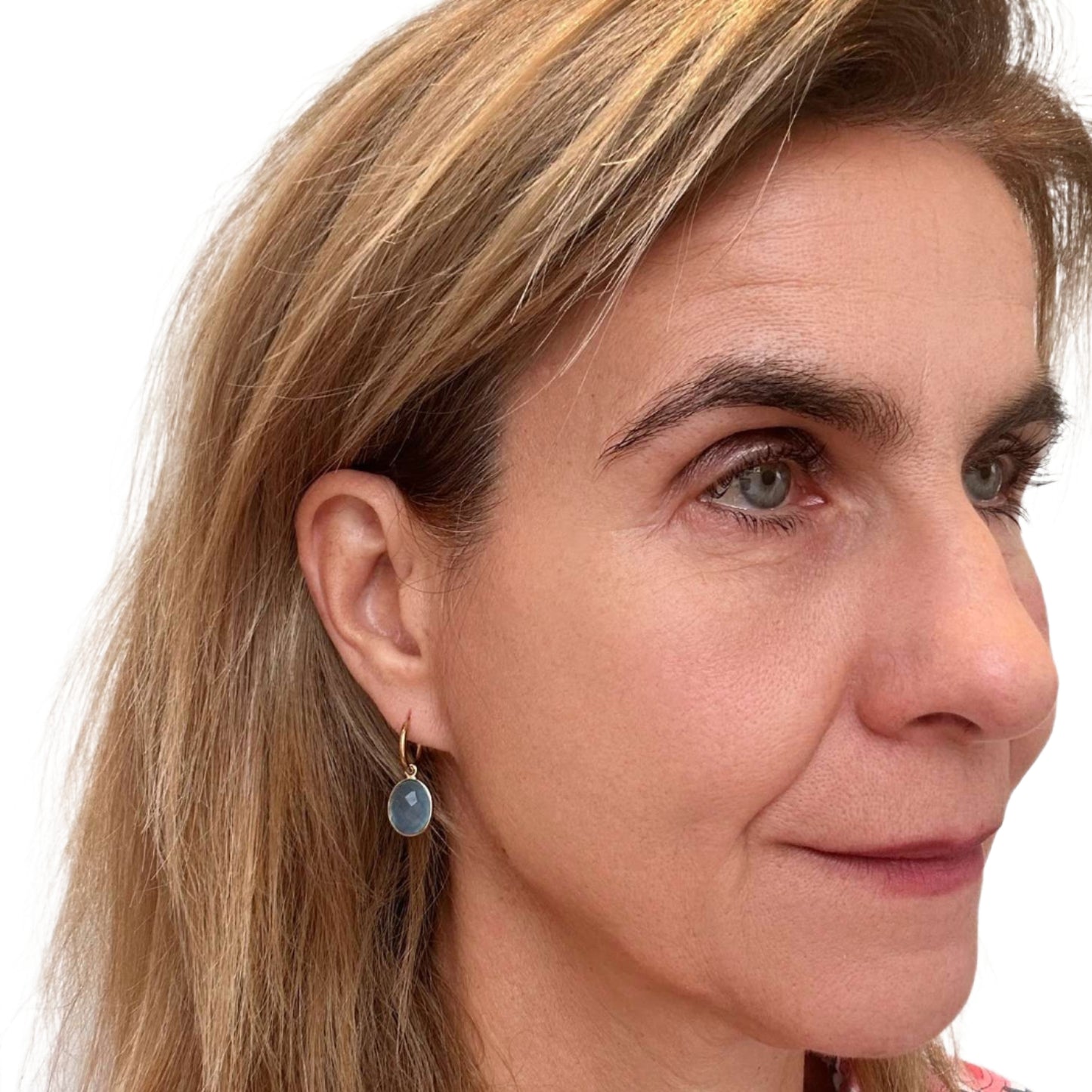 Woman wearing gold hoop earrings with Blue Chalcedony gemstone oval charms