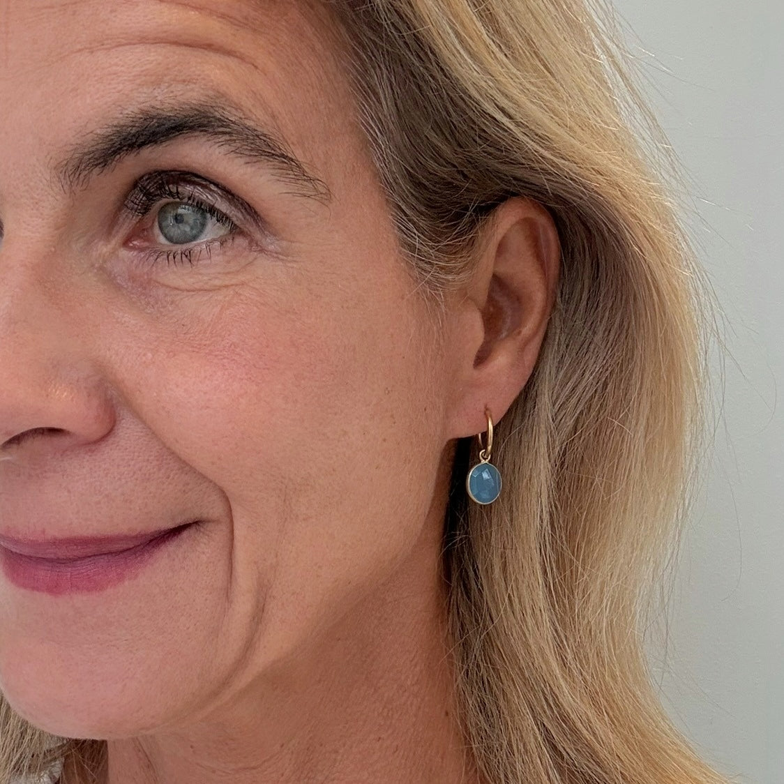 Close-up of a woman wearing a gold earring with a blue gemstone against a neutral background
