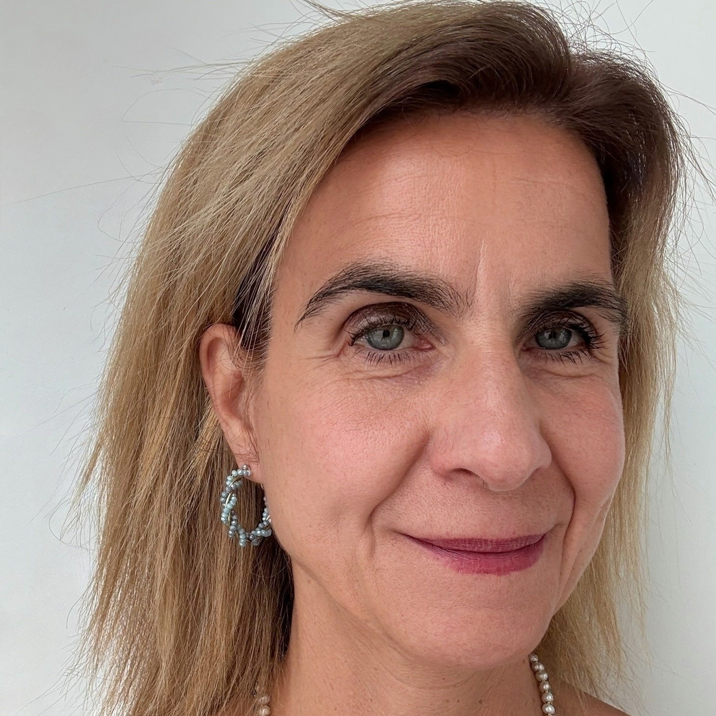 Big beaded hoop earrings are twisted gold with light and grey blue beads worn on model