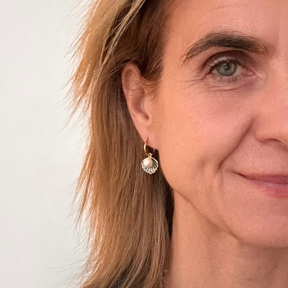 Delicate gold hoop earrings with a pretty blue clam and pearl charms on model