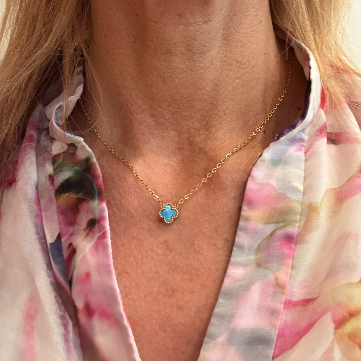 Delicate gold chain necklace with tiny 9mm blue clover charm in the middle worn on model