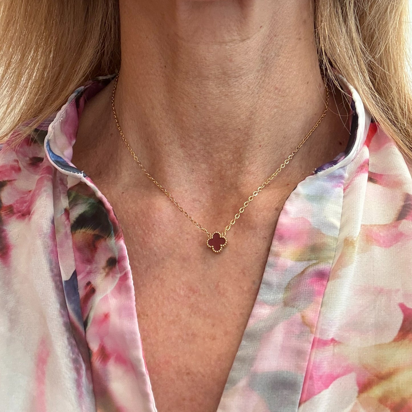 Delicate gold chain necklace with tiny 9mm burgundy clover charm in the middle worn on model