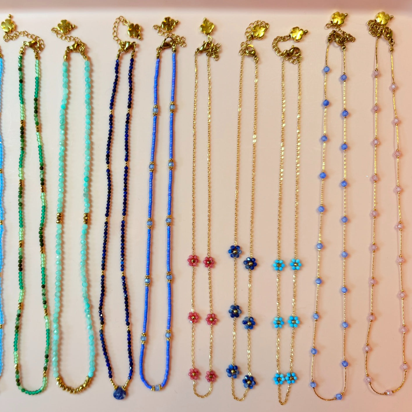 Set of beaded necklaces with floral accents on a light pink background