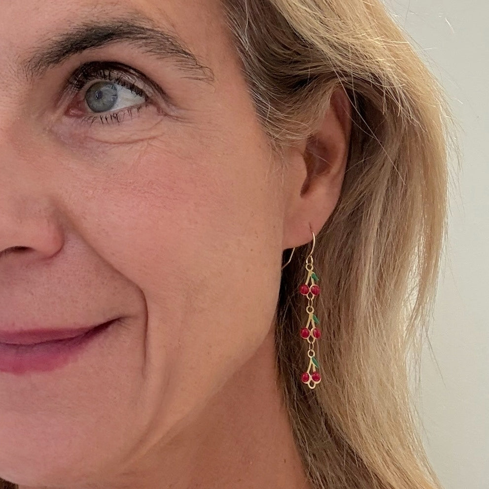 Close-up of a woman wearing a gold earring with cherry charms against a neutral background