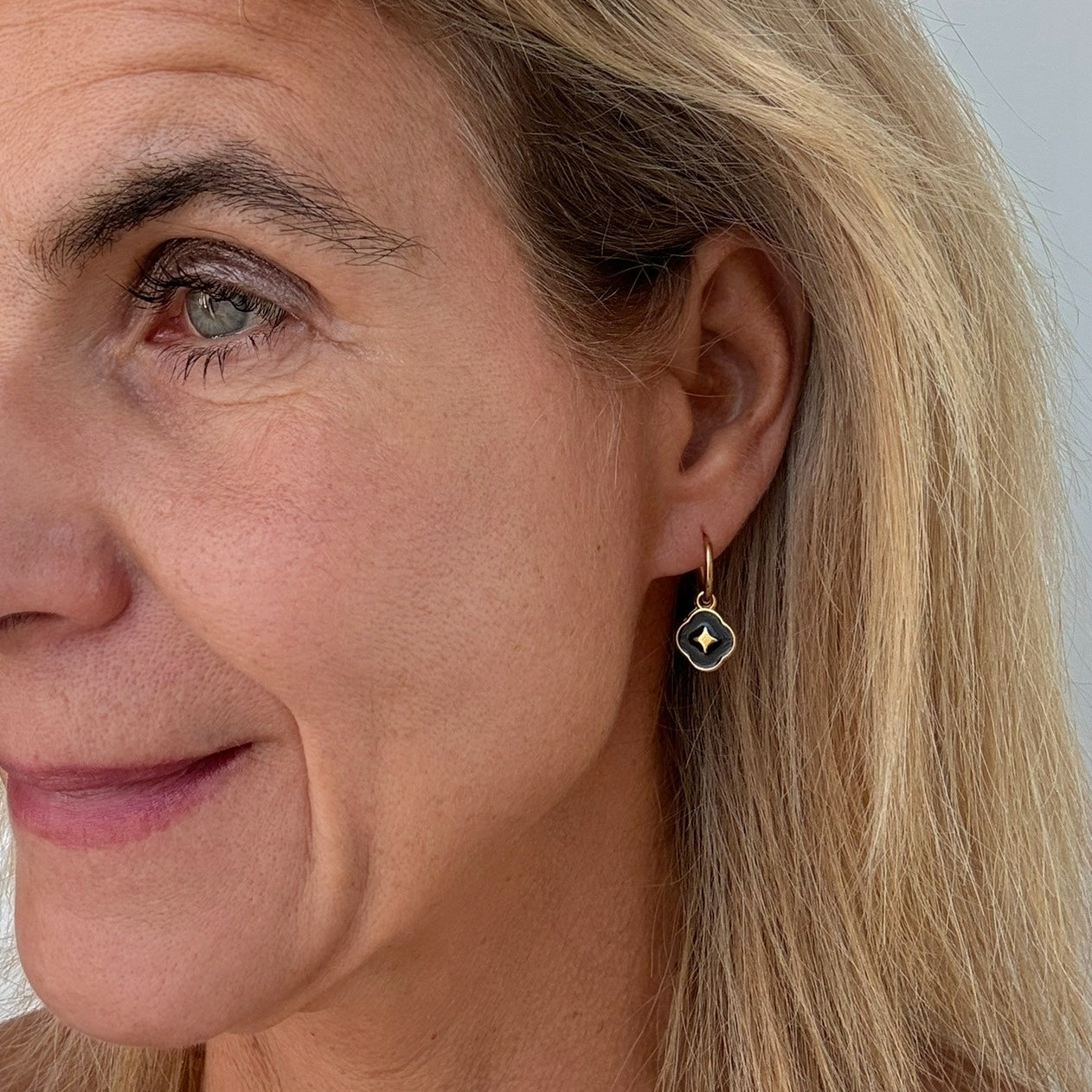 Gold hoop earrings with a clover shaped black enamel charm worn on woman