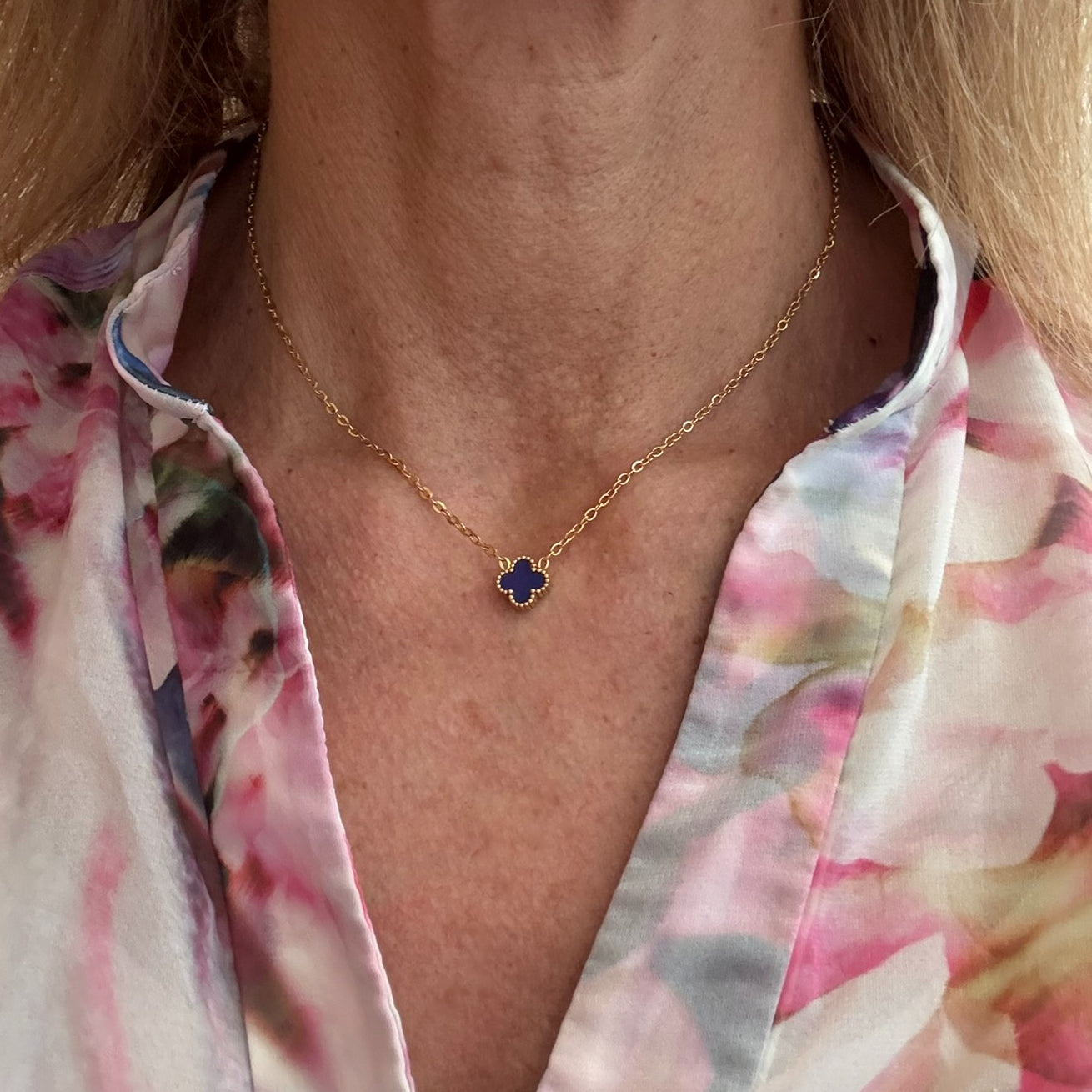 Delicate gold chain necklace with tiny 9mm dark blue clover charm in the middle worn on model