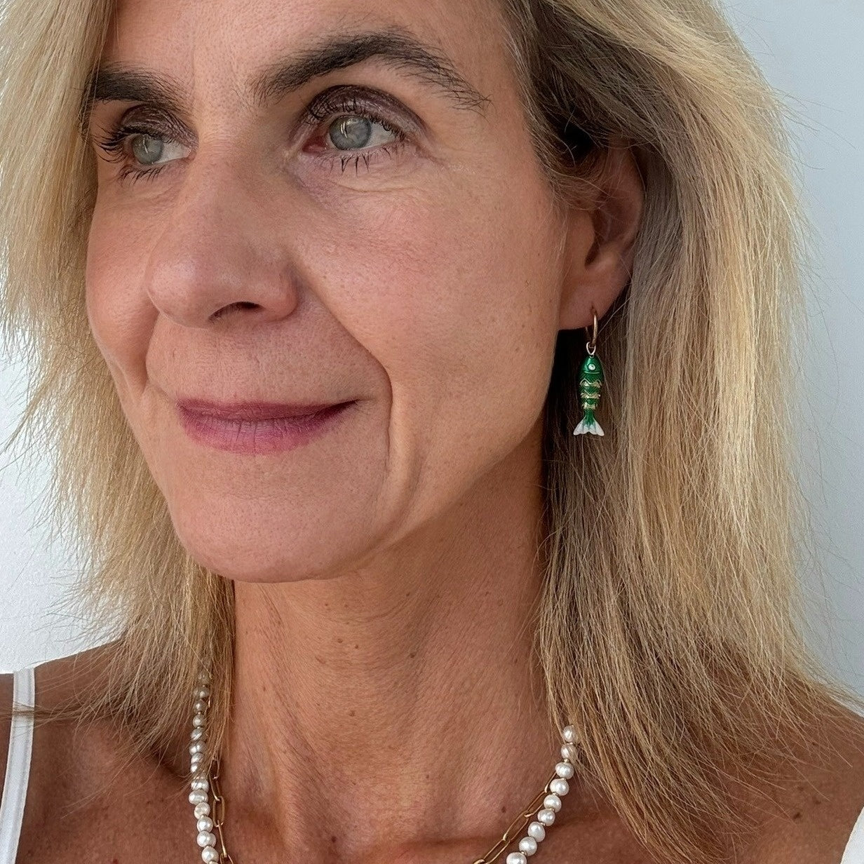 Close-up of a woman wearing green fish-shaped earrings with a plain background