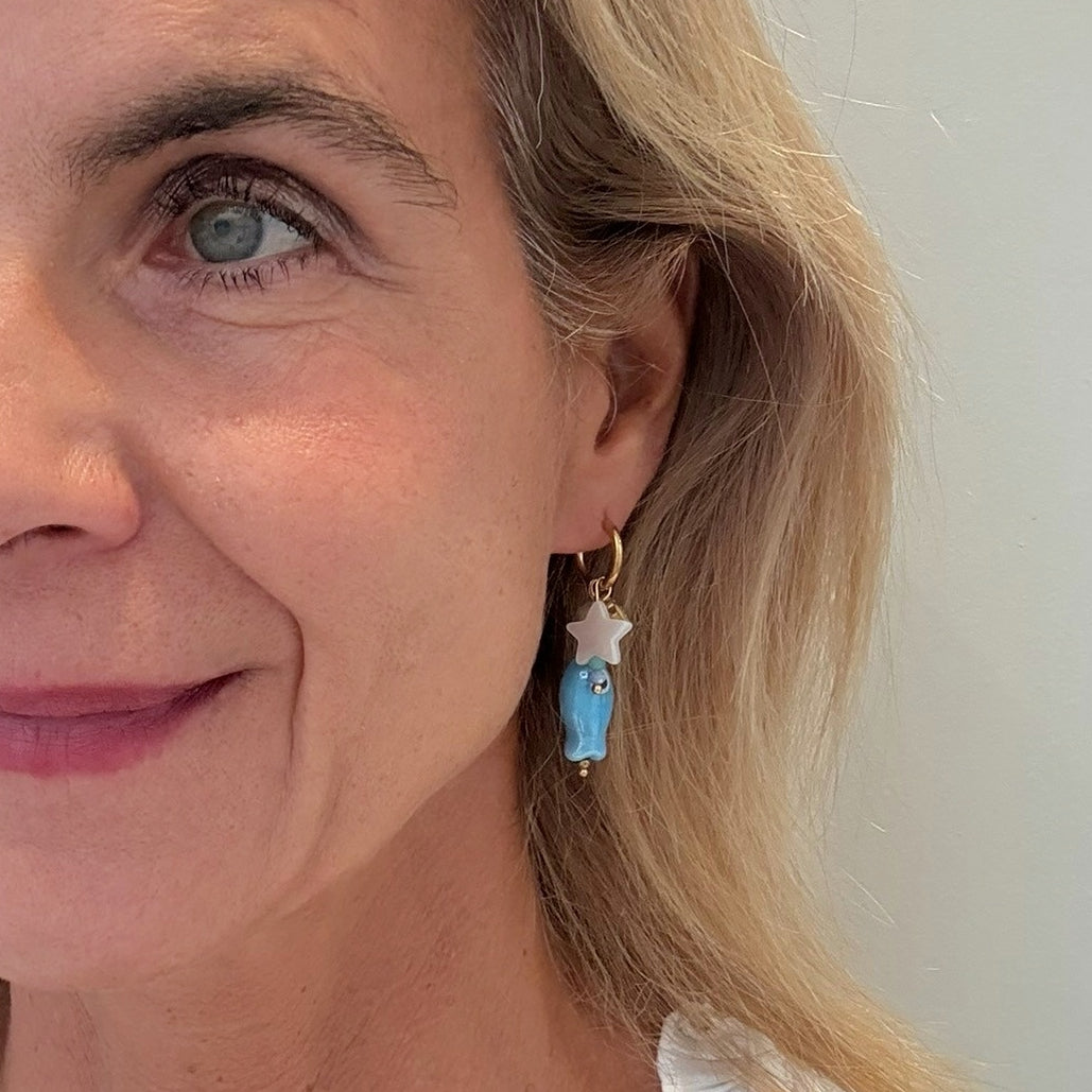 Close-up of a woman wearing a fish/shell/star-shaped earring with a blue bead.