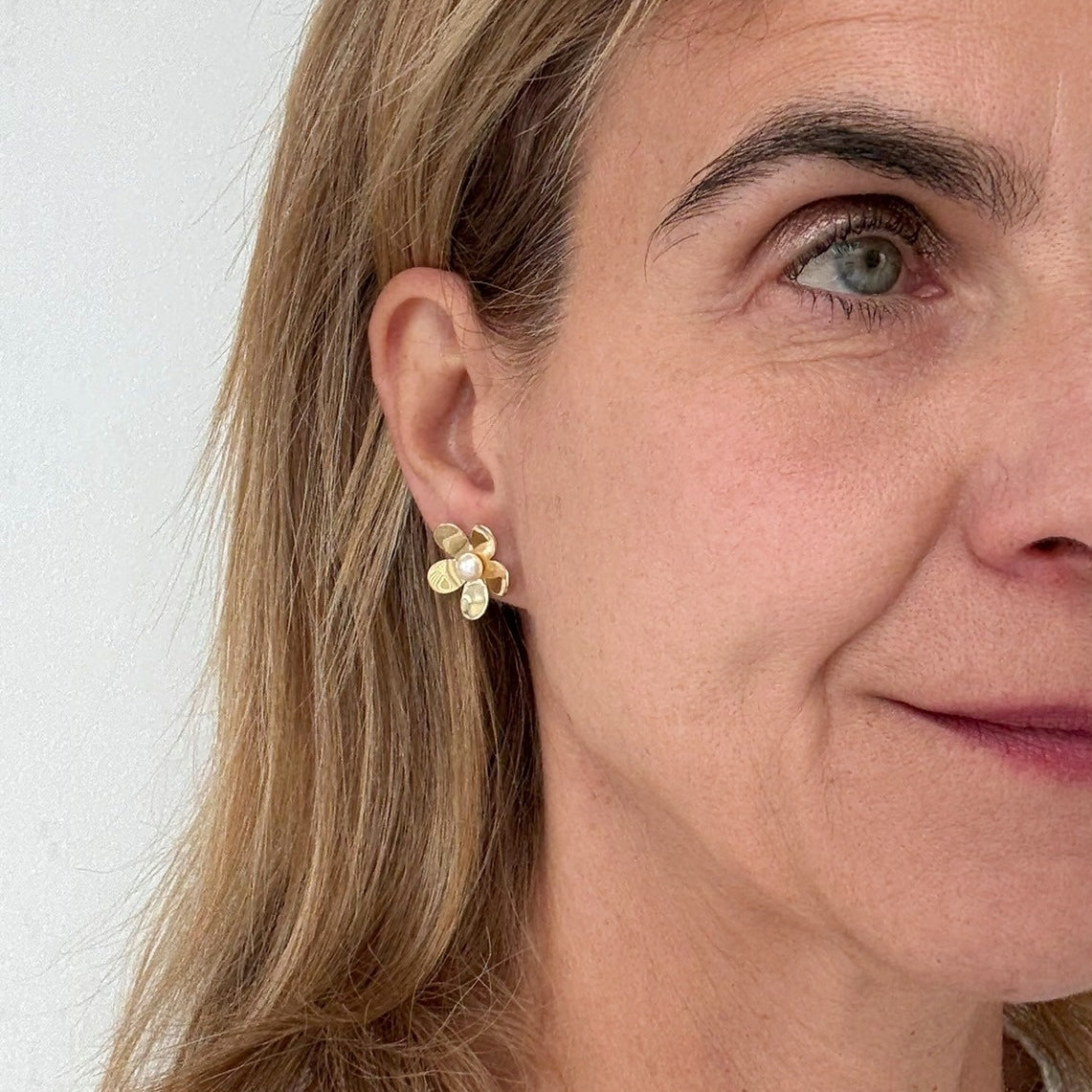 ese stud earrings are in the shape of a flower with a freshwater pearl in the centre worn on model