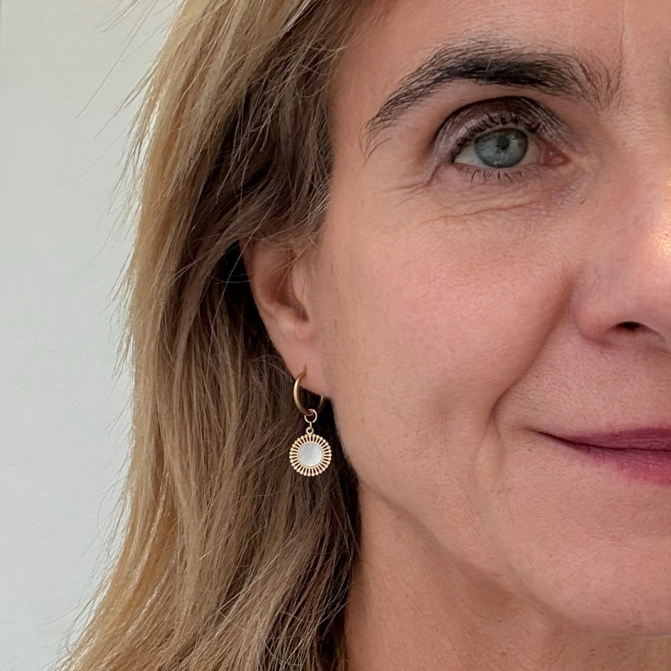 Gold hoop earrings with mother of pearl and small gold round shaped charms worn on model