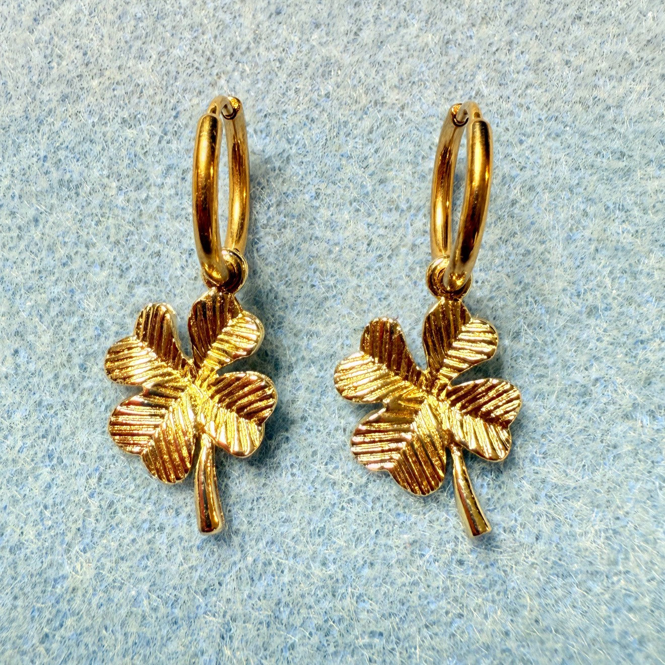 Delicate gold hoop earrings with pretty gold clover charms on blue background