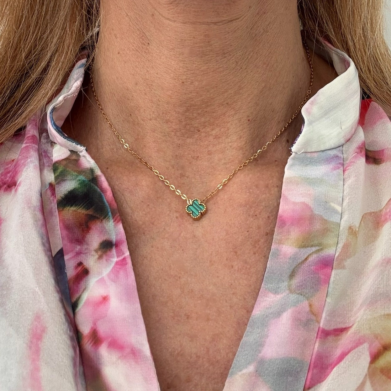 Delicate gold chain necklace with tiny 9mm green clover charm in the middle worn on model