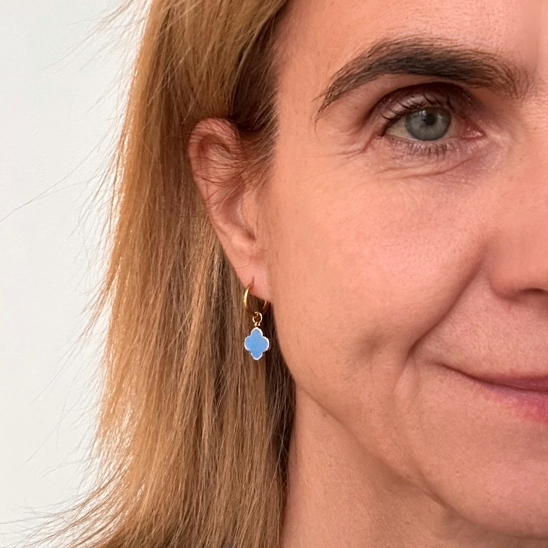 Delicate gold hoop earrings with enamel cornflower blue clover charms worn on model