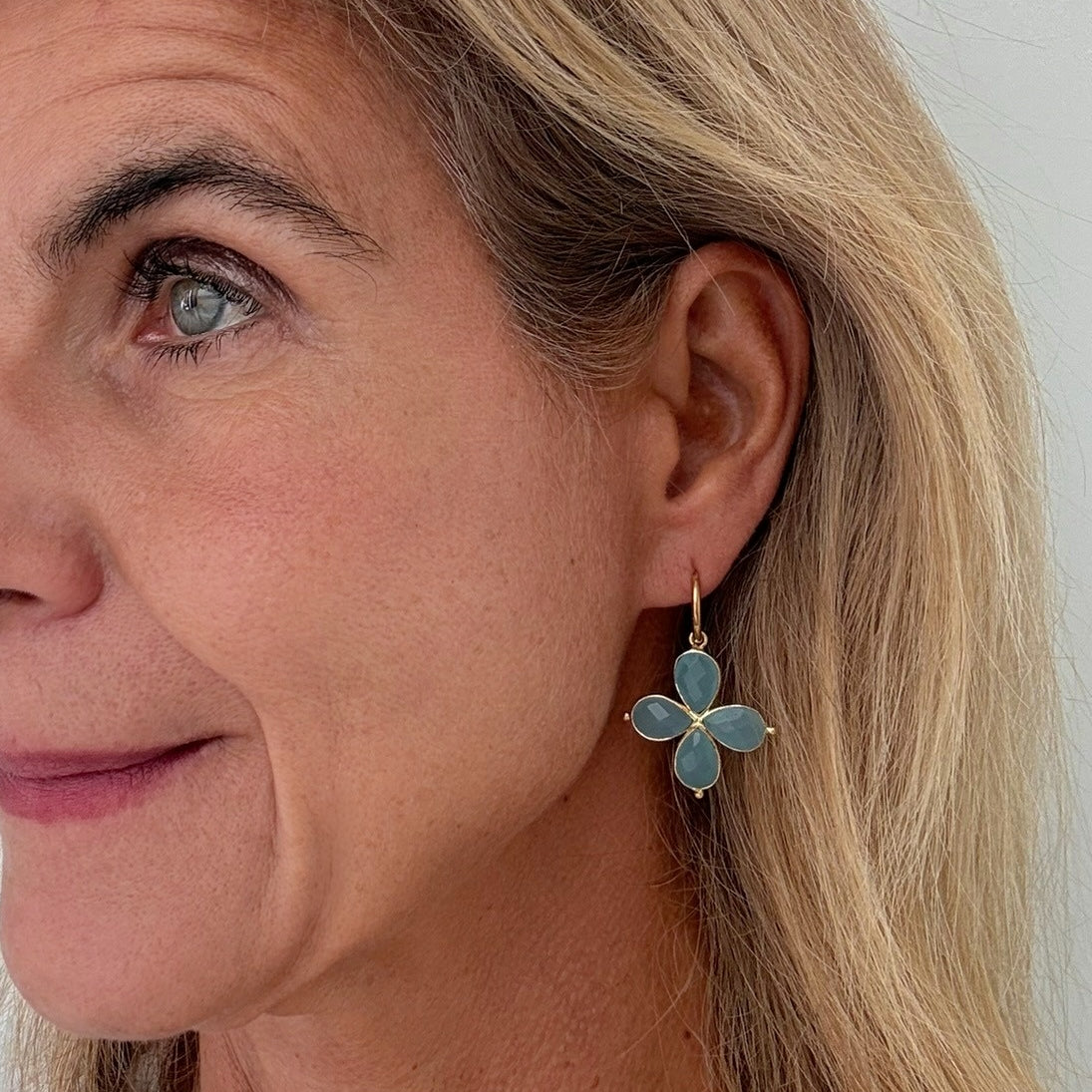 Close-up of a woman wearing gold hoop earroings with flower-shaped aqua hydro quartz gemstones.