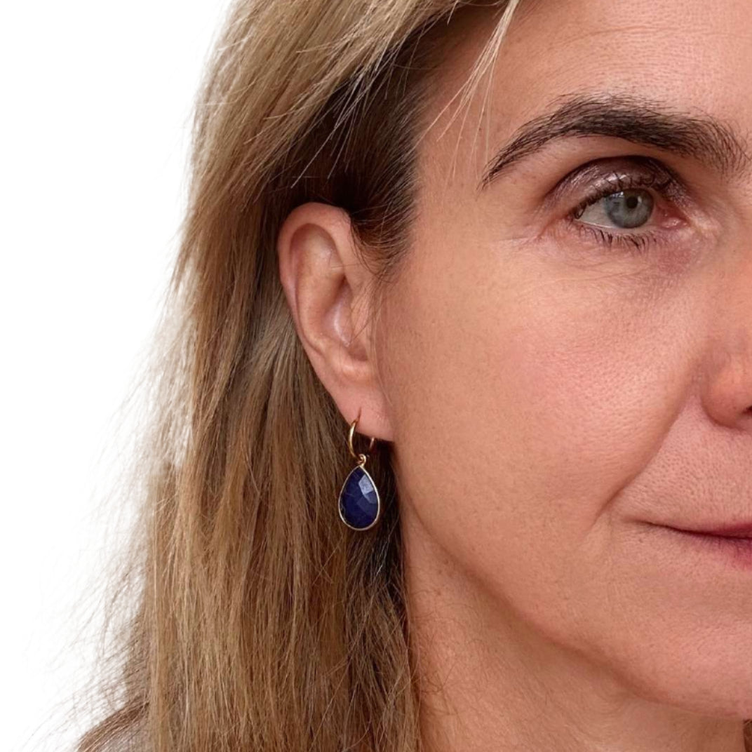Close-up of a woman wearing lapis lazuli gemstone earrings with a neutral background