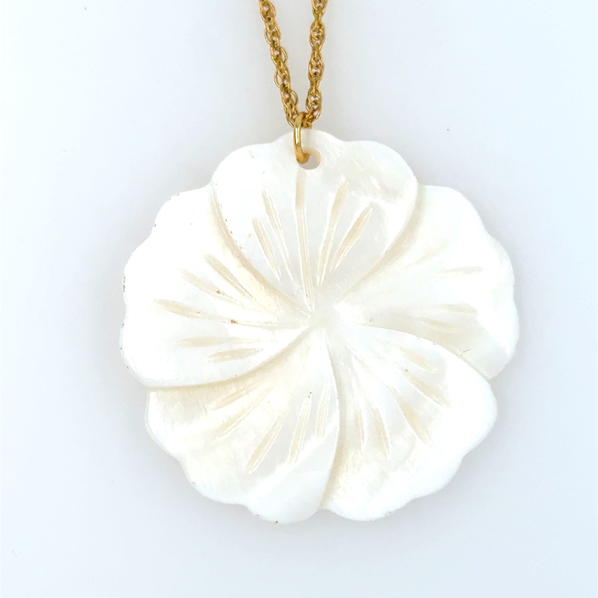 close up of pendant in mother of pearl in shape of a flower which is part of a gold chain necklace