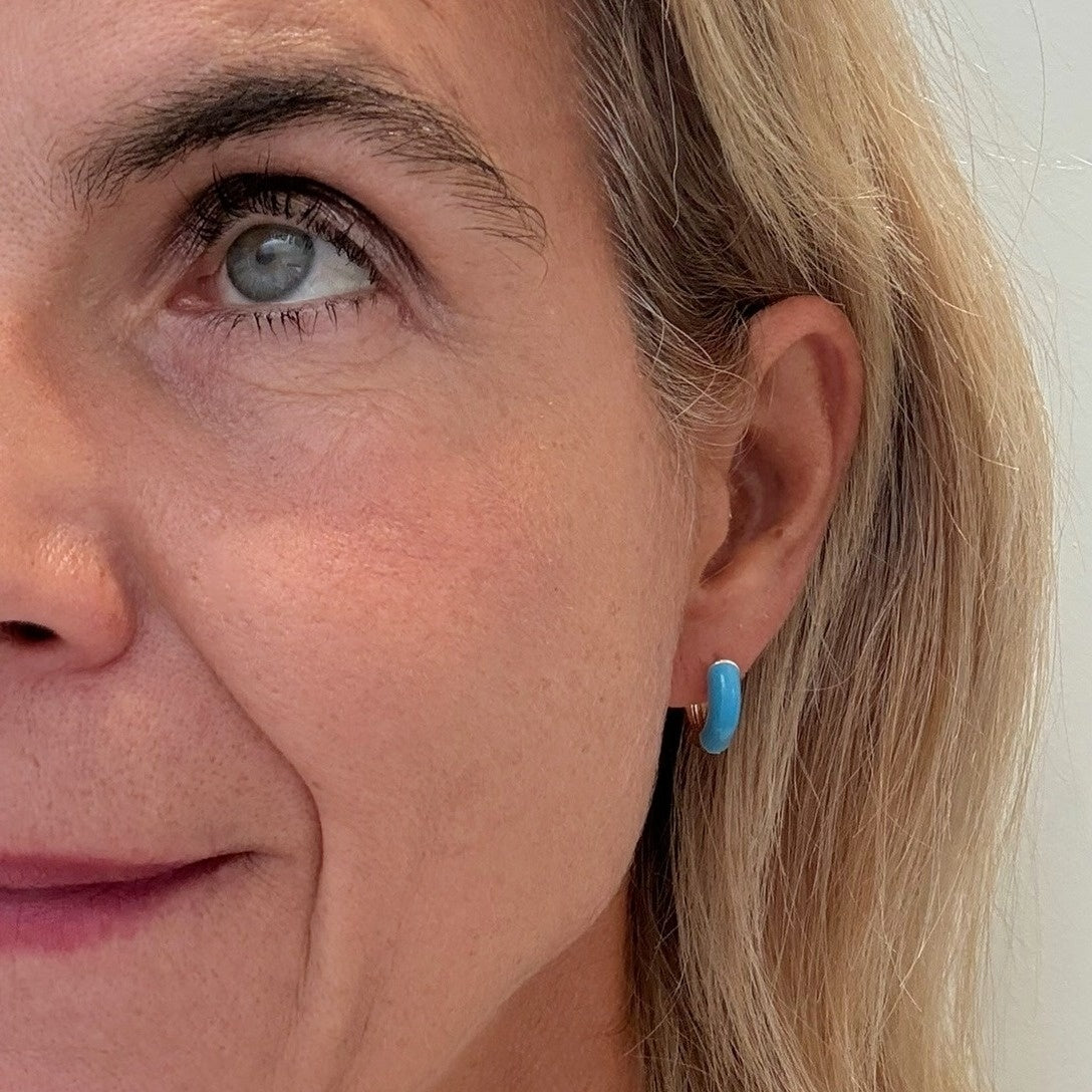 Close-up of a person wearing a blue enamel earring with a neutral background
