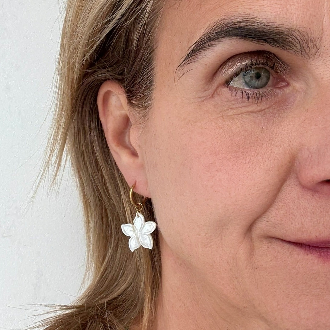 woman wearing hoop earrings with white flower shaped mother of pearl charms