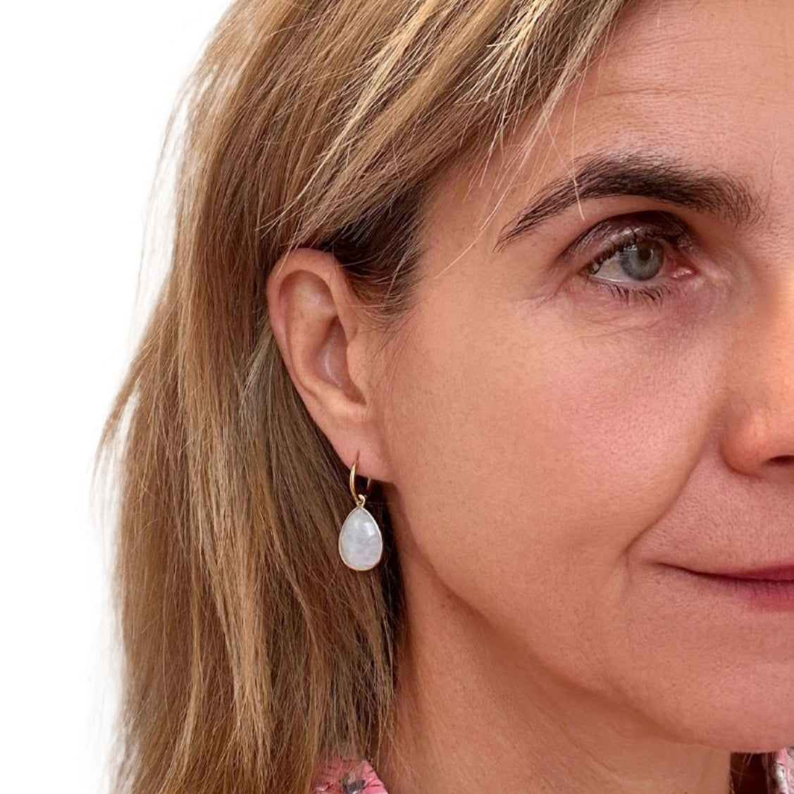 Close-up of a woman wearing moonstone hoop charm earrings with a neutral background