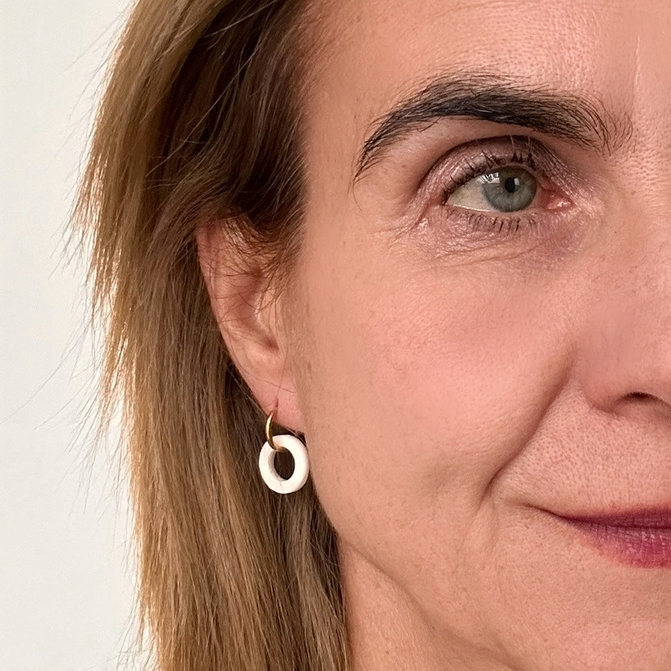 Delicate gold hoop earrings with circle shaped charm in white mother of pearl shell on model