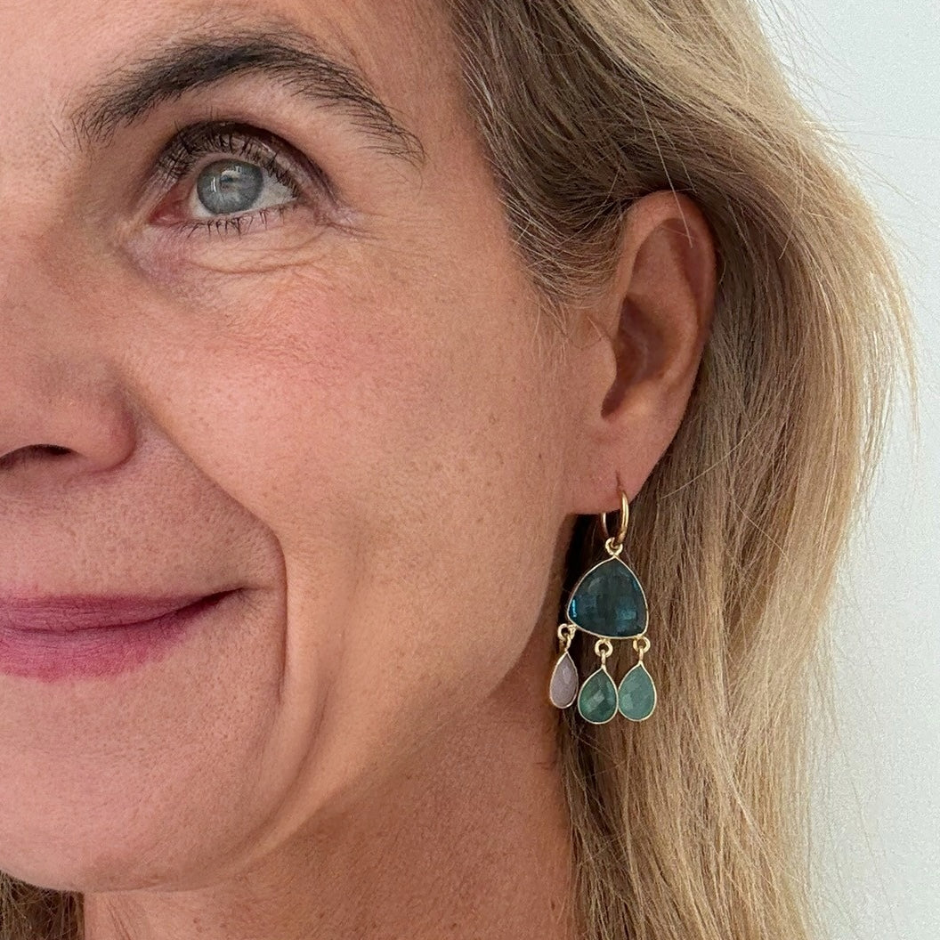 Woman wearring gold hoops with medley of pastel coloured dangling gemstone charms