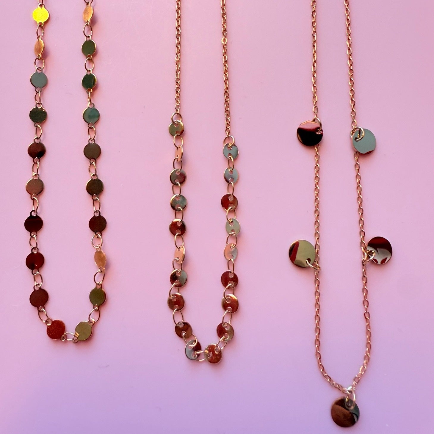 three shimmering gold necklaces with round disc chains in different styles