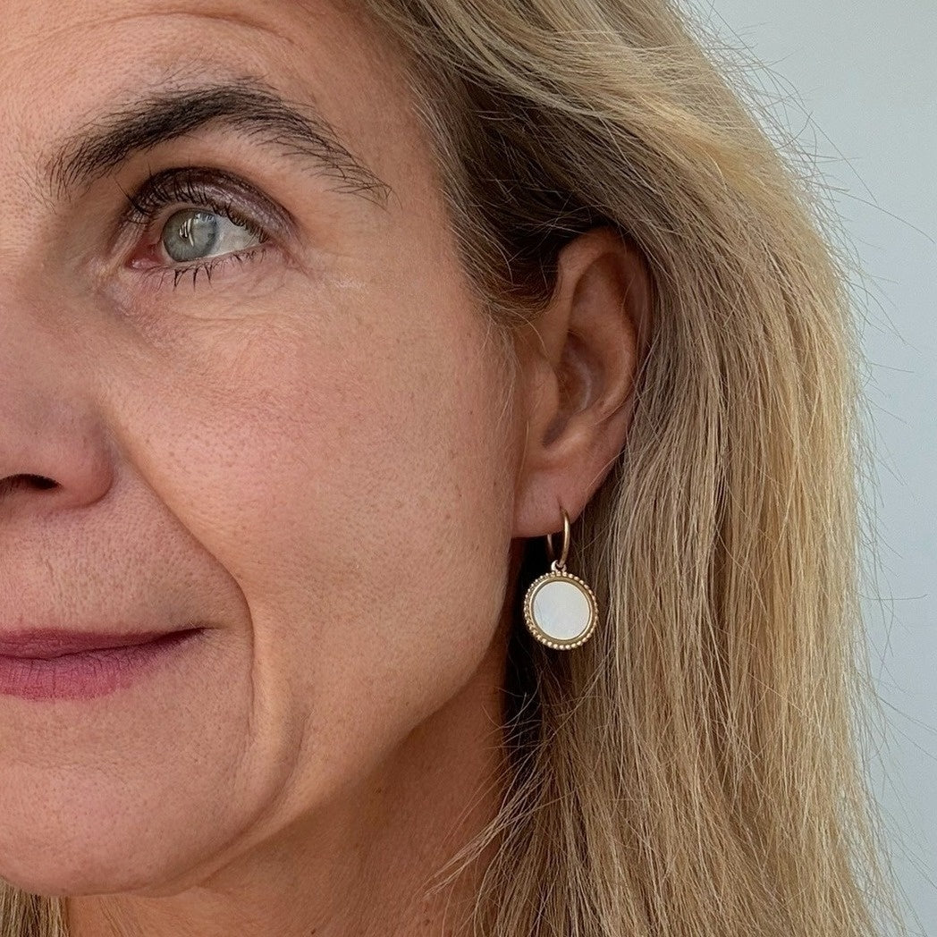 woman wearring Gold hoop earrings with large mother of pearl and gold patterned round charms