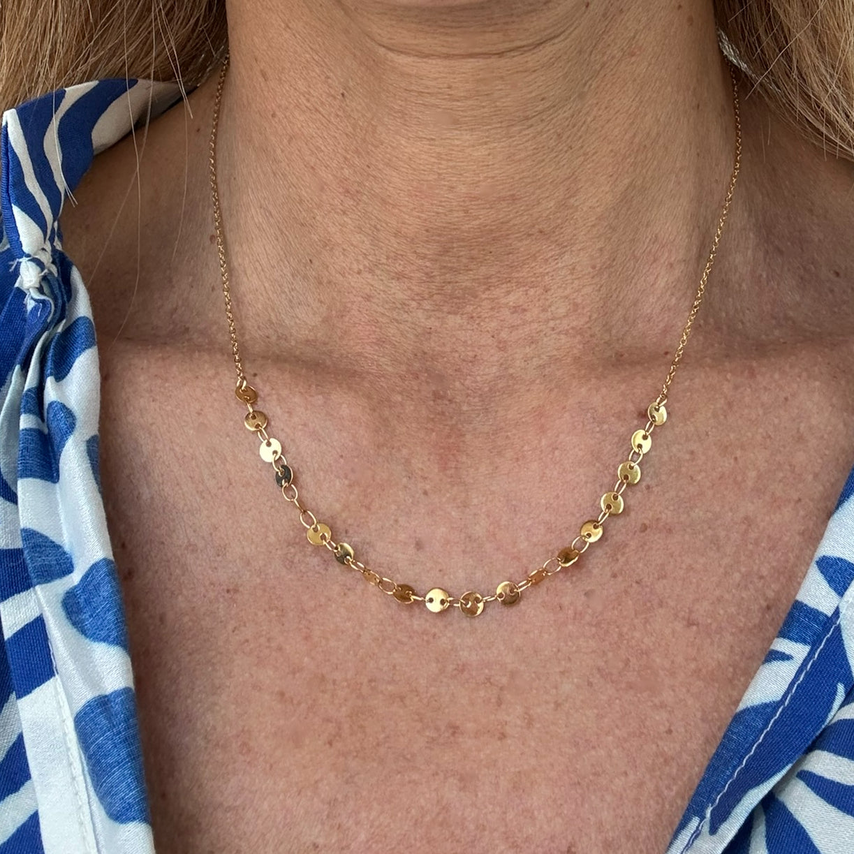 Delicate chain necklace with small oval discs worn on model.