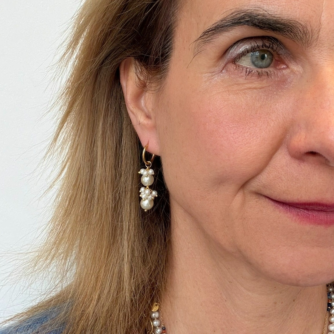Close-up of a woman wearing pearl earrings with a plain background