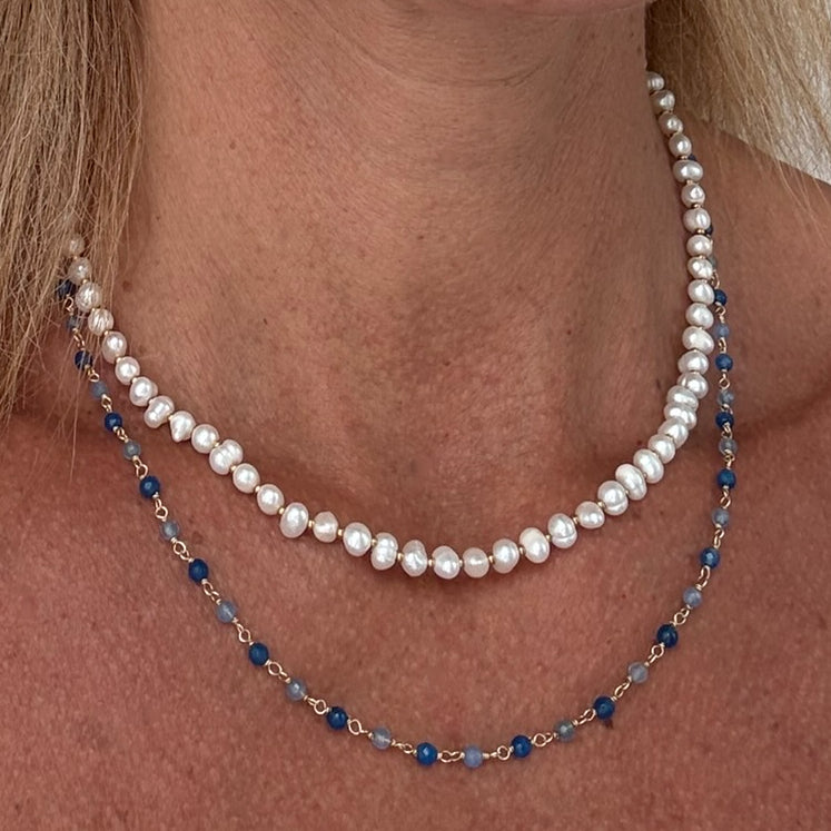 Two necklaces, one with freshwater pearls and gold beads, the other with blue topaz gemstone beads worn on a model