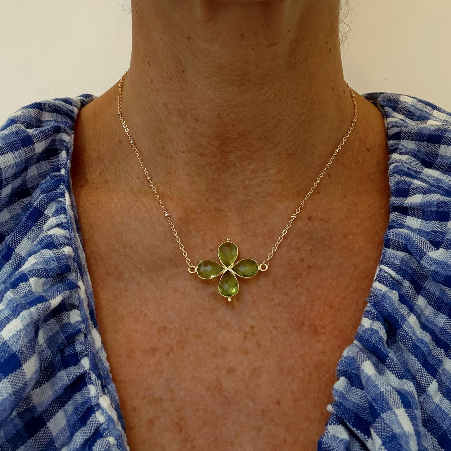 Delicate gold chain necklace with a Peridot gemstone four petal flower shaped charm worn on model