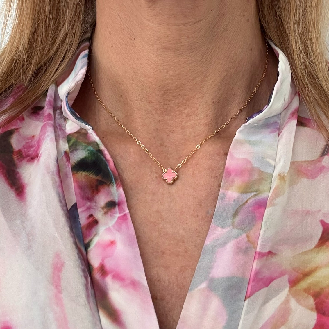 Delicate gold chain necklace with tiny 9mm pink clover charm in the middle worn on model