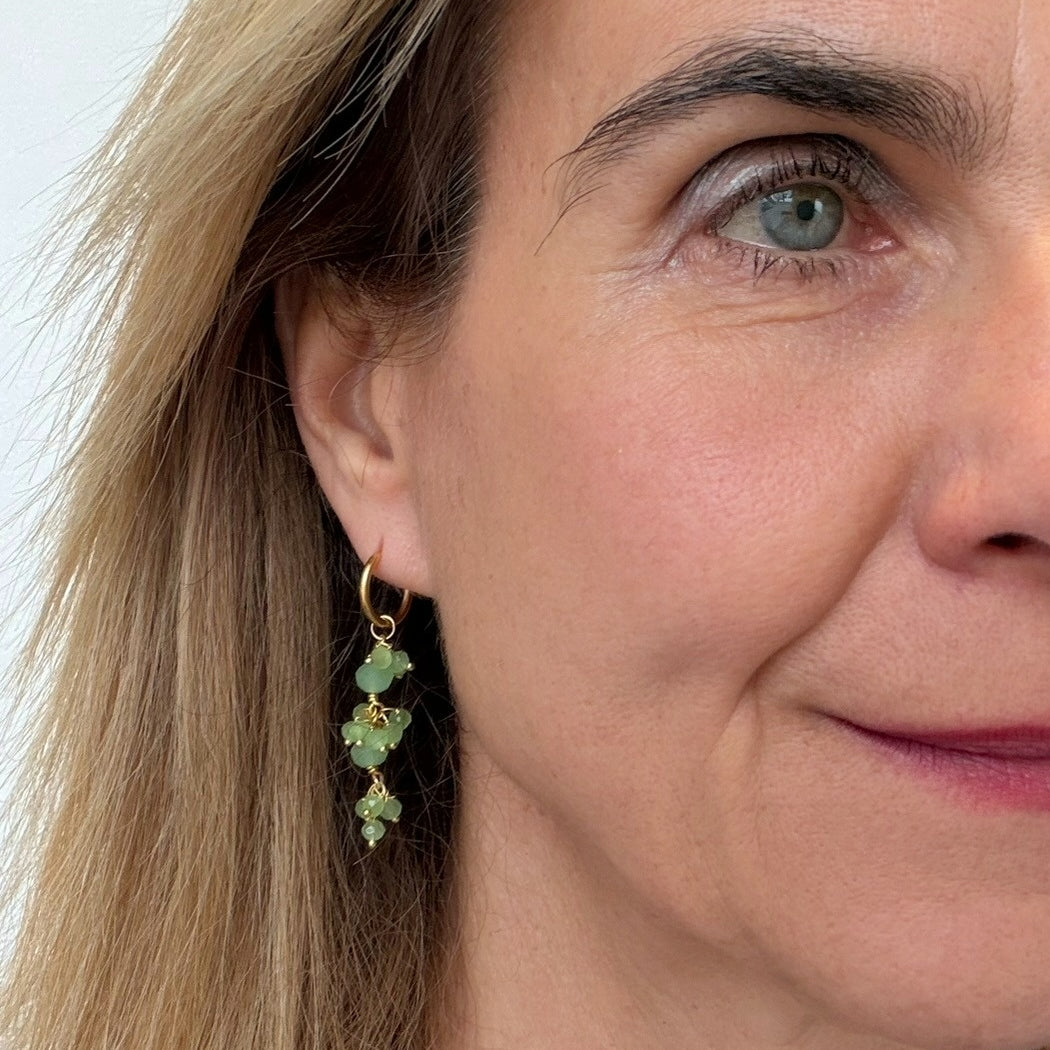 Close-up of a woman wearing green gemstone earrings with a neutral background