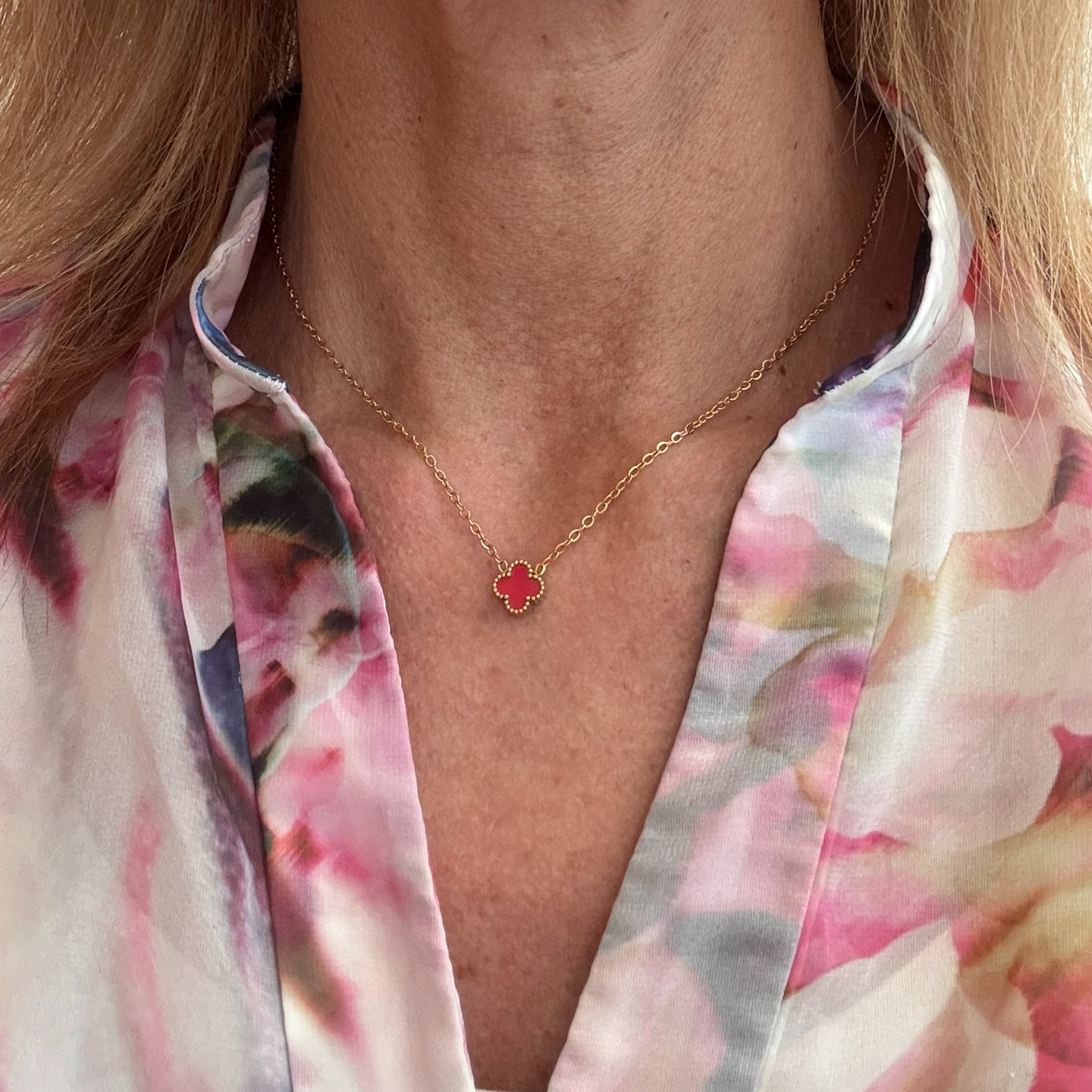 Delicate gold chain necklace with tiny 9mm red clover charm in the middle worn on model