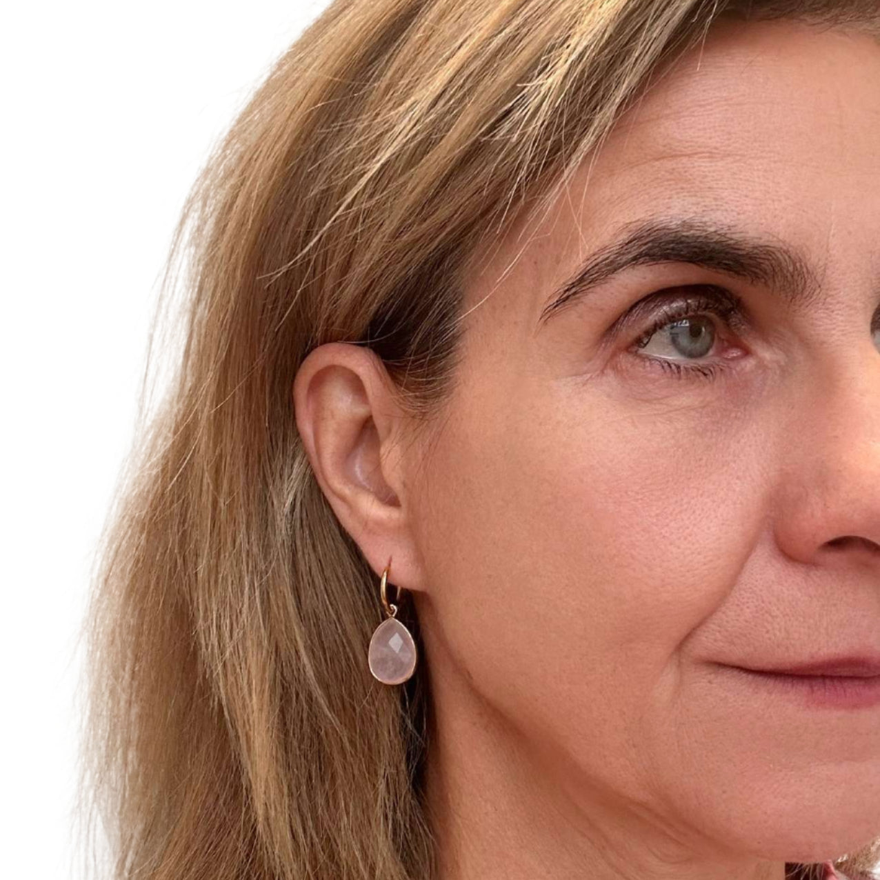 Close-up of a woman wearing gold hoop earrings with Rose Quartz semi-precious gemstone teardrop charms