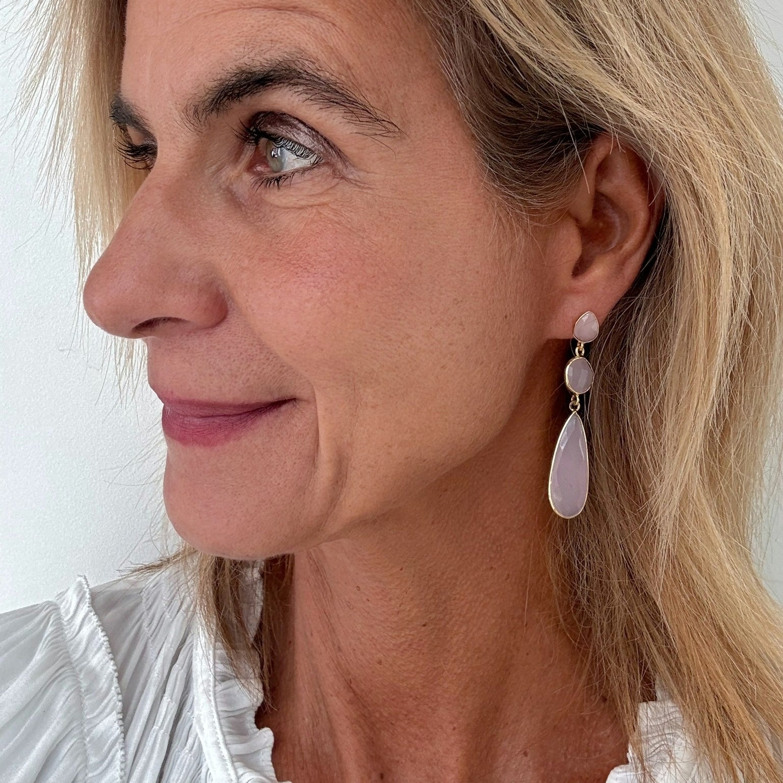 Close-up of a woman wearing a pair of Rose Quartz three stone dangling earrings with a white background