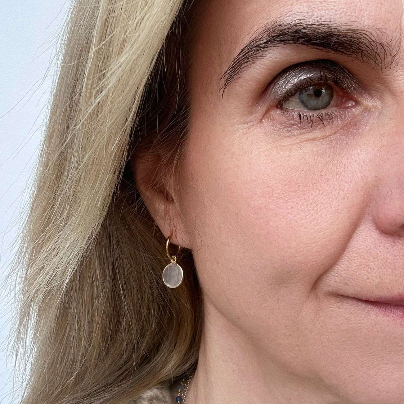 Close-up of a woman wearing a gold earring with rose quartz gemstone charm.