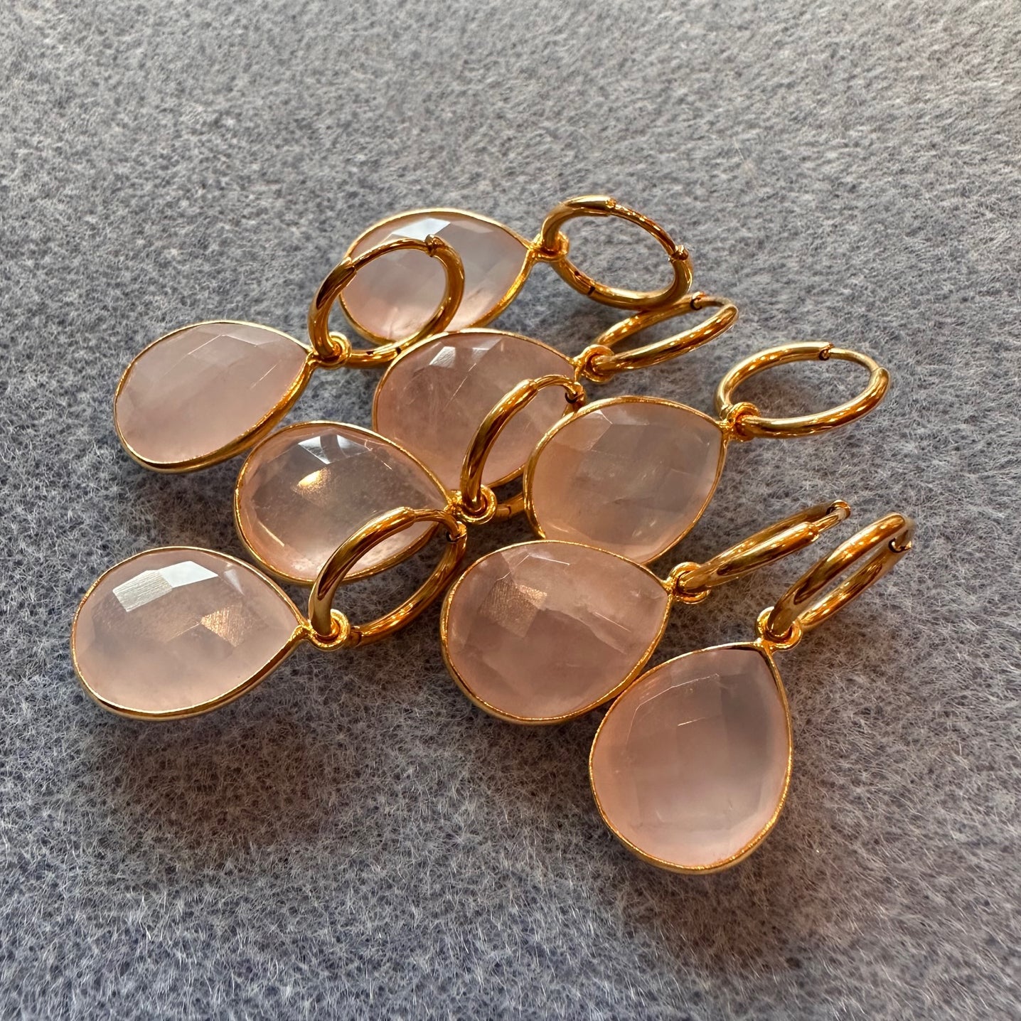 Gold and rose quartz earrings on a gray surface