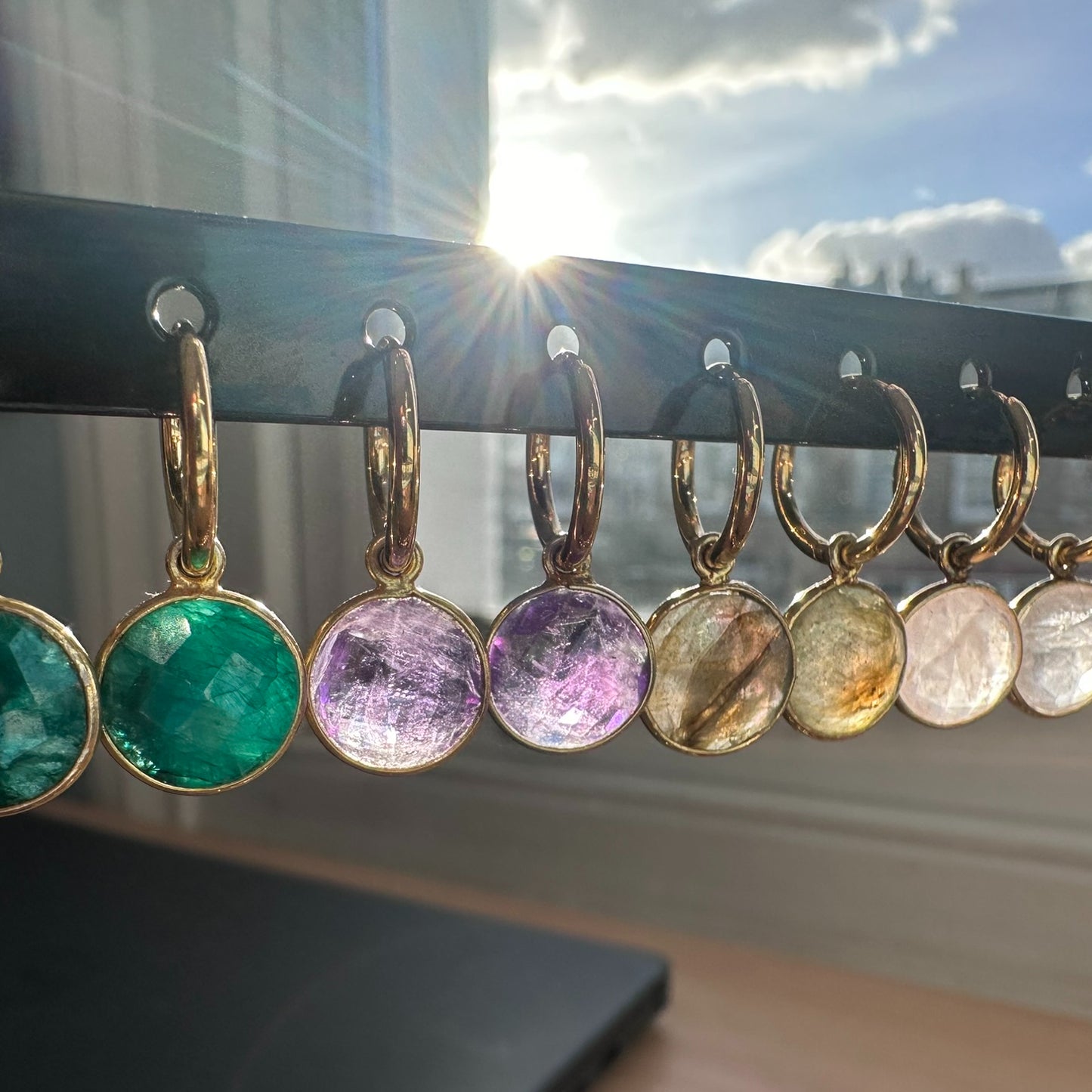 Set of colorful gemstone earrings on a black stand with sunlit window in the background