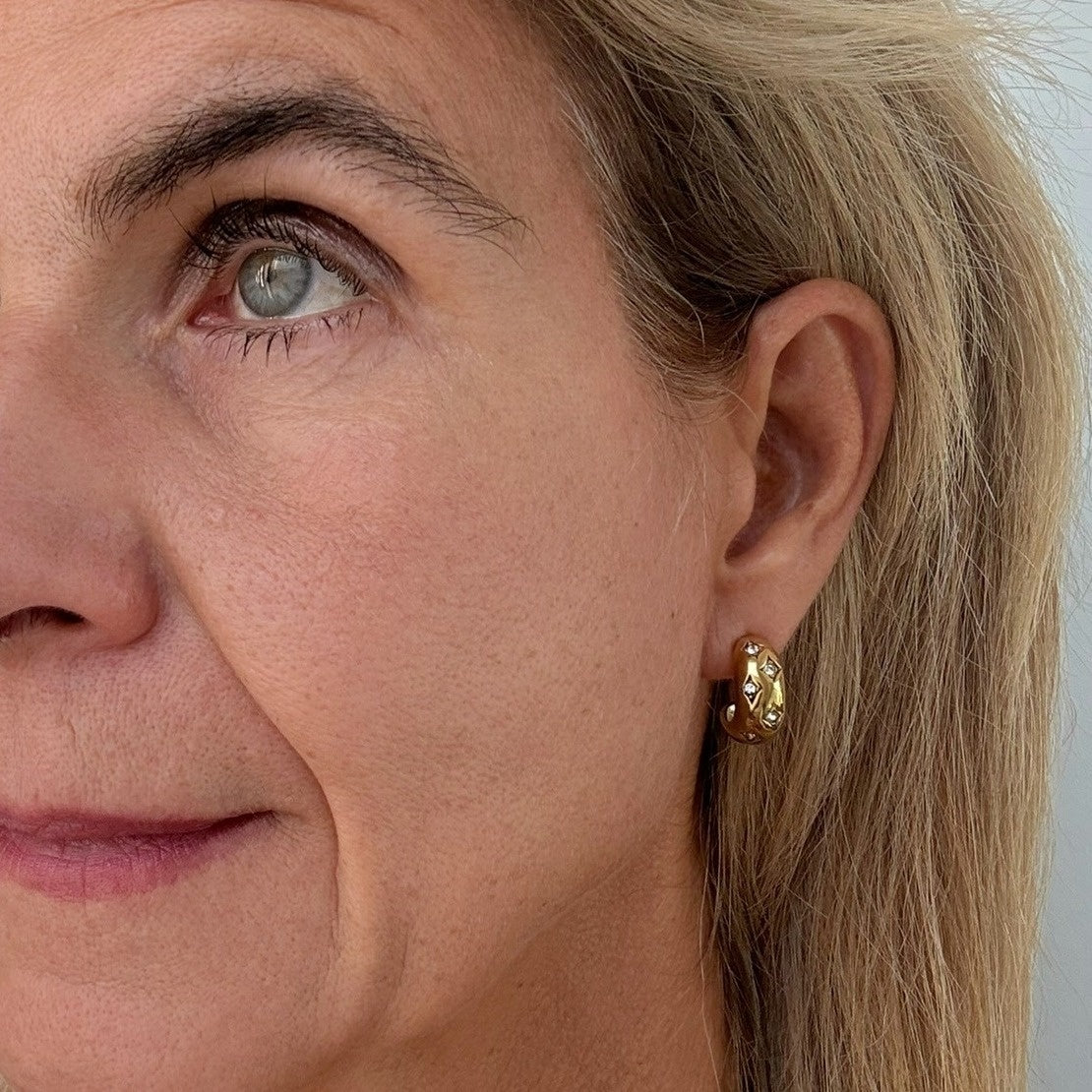 Woman wearing gold rounded earrings with small crystals